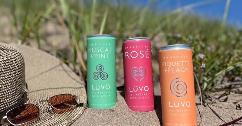 LUVO Muscat + Mint Spritzer, Sparkling Rosé, and Piquette + Peach Spritzer on sandy beach with sun hat and sunglasses